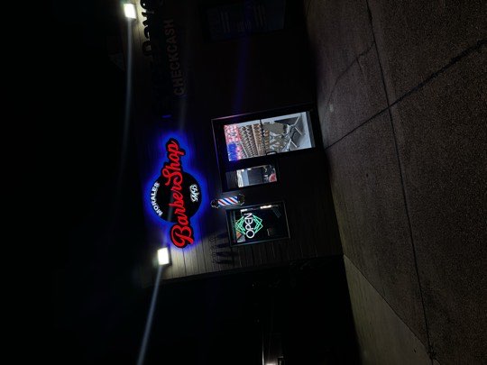 Front of Morales Barbershop MB at night, with the sign and the open sign lit.