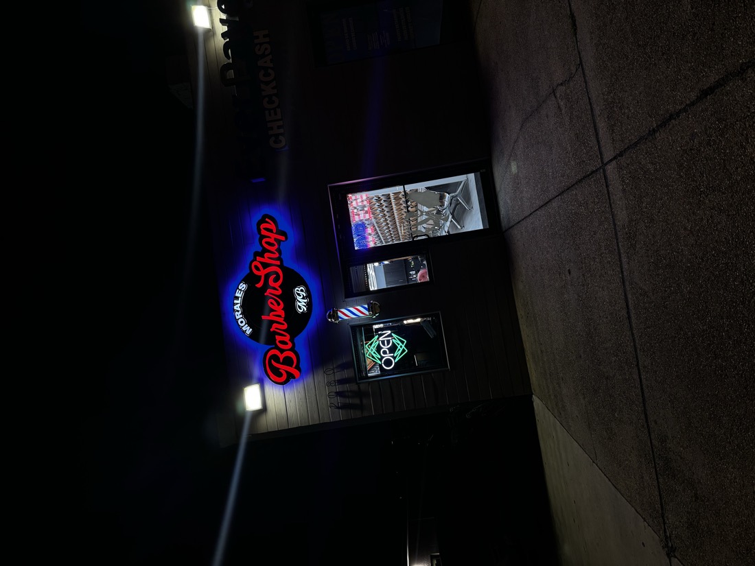 Front of Morales Barbershop MB at night, with the sign and the open sign lit.