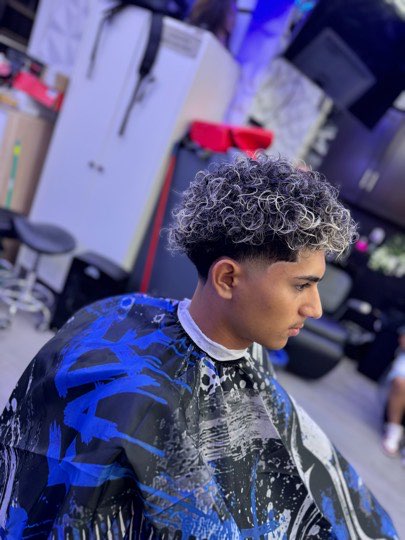 Curls with platinum highlights on top and a mid fade on the sides.