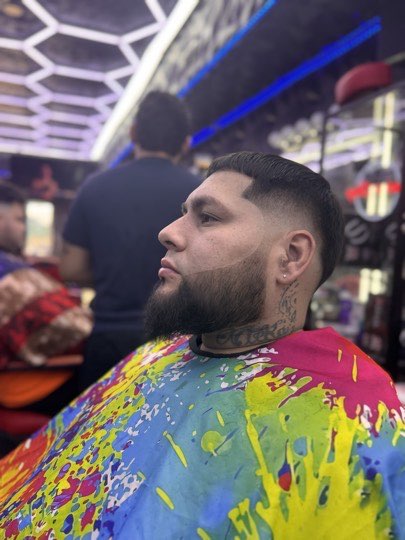 Skin fade with a tight full beard and a straight line up on the forehead.